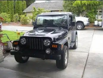 A damaged black Jeep parked in a driveway.